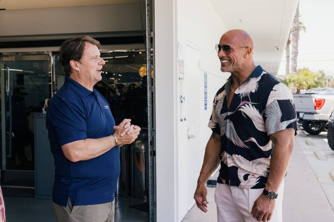 Dwayne “The Rock” Johnson and Jim Farley smile in conversation with each other.